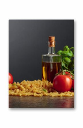 Fusilli pasta with olive oil, tomatoes and basil on a black background.