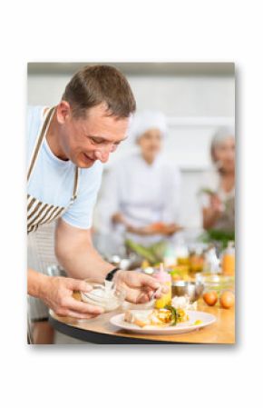 Adult man in apron pours sauce into ready dish at cooking master class