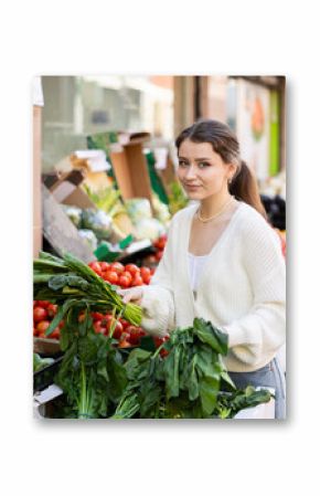 Young woman buyer choosing fresh spinach at vegetable market
