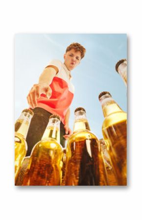 Young man choosing beer bottle from outdoor cooler under summer sky, low angle. Concept of alcohol tourism, festivals, lifestyle promotion, event marketing and leisure branding.