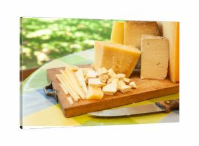 Assortment of sliced and chunked cheeses with knife on wooden cutting board