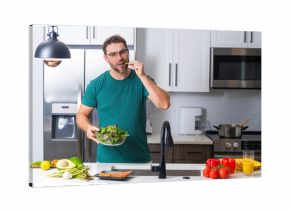 Young man cooking vegan healthy salad in kitchen. Millennial man at modern kitchen table chop vegetables, prepare fresh vegetable salad for dinner or lunch. Healthy diet, vegetarian concept.