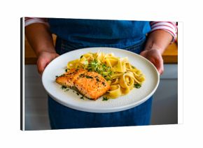 Woman holding plate with pasta with baked salmon steak, close-up
