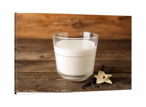 Glass of fresh vanilla milk with sticks and flower on wooden background