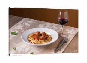 Plate of spaghetti and meatballs accompanied by a glass of red wine on a rustic wooden surface