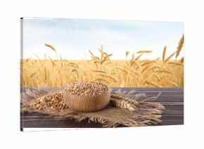 Cereal grains and ears of wheat on wooden table against agricultural field