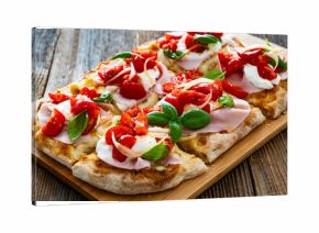Pinsa Romana with boiled ham, cherry tomatoes, burrata cheese and basil leaves on wooden table 