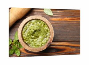 Fresh pesto sauce in mortar, pestle and basil leaves on wooden table, flat lay. Space for text