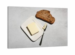 Slice of fresh bread, dish with butter and knife on grey grunge background