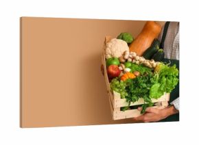 Male farmer with box of vegetables and fruits on beige background with space for text, closeup