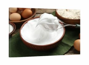 Whipped egg whites in bowl, whisk and ingredients on wooden table, closeup