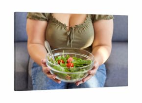 Fat woman eating healthy food. Cropped shot of chubby plump overweight girl sitting on couch holding glass bowl of fresh vegetable salad. Healthy diet and weight loss concept