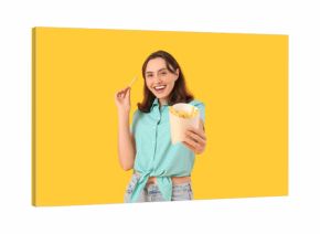 Beautiful young woman with french fries on yellow background