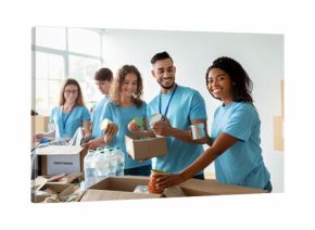 A diverse group of volunteers smiles while sorting donated food at a community charity donation center. They prepare boxes filled with essentials for those in need.