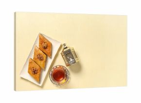 Glass of tasty Turkish tea with baklava and fanoos on beige grunge background. Ramadan celebration