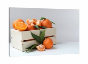 Fresh tangerines and green leaves in crate on white wooden table, space for text