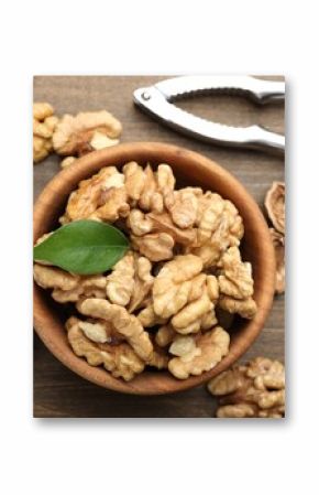 Peeled walnuts in bowl and nutcracker on wooden table, flat lay