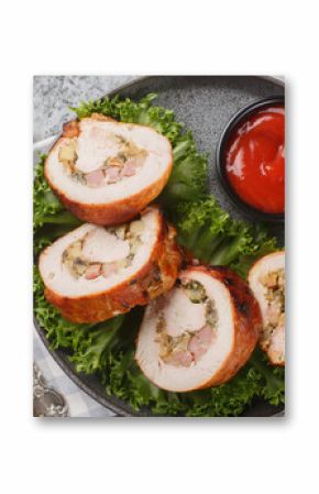 Festive sliced ​​turkey fillet roll with bacon, onions and mushrooms served with ketchup close-up in a plate on the table. Horizontal top view from above