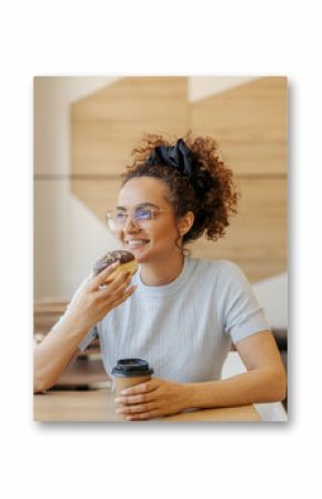 Portrait of smiling young woman enjoying sweet doughnut and coffee in fast food restaurant.