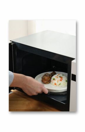 Woman putting plate with food into microwave oven at wooden table indoors, closeup