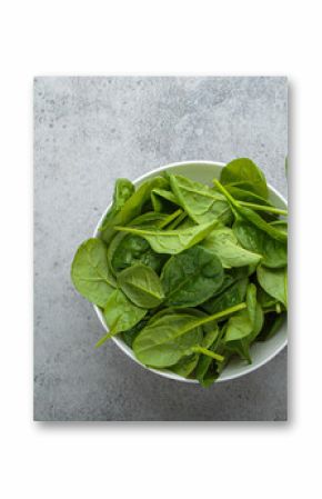 Fresh spinach leaves in a white bowl set on a gray backdrop, showcasing their vibrant green color and healthy appeal, perfect for salads, smoothies, or side dishes. Copy space
