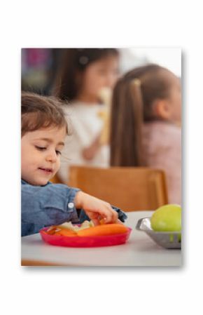 Young girl enjoys a healthy snack at preschool while other children sit nearby, promoting healthy eating habits, nutrition, and diversity in an early childhood classroom setting.