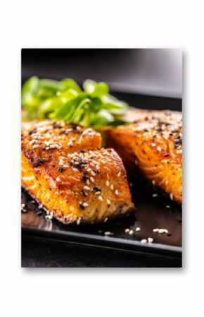 Two salmon fillets baked until crispy, sprinkled with sesame on a black plate.