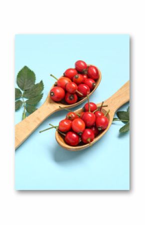 Wooden spoons with fresh rose hip berries and leaves on blue background
