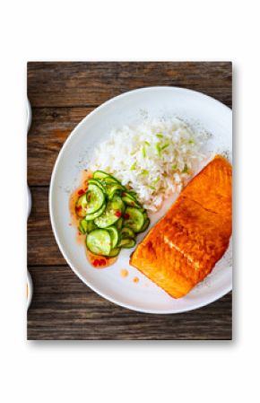 Seared salmon steak with boiled white rice and sliced cucumber on wooden table 