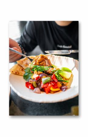 Close-up of a person enjoying a colorful and appetizing dish with vegetables and meat, garnished with fresh herbs. Perfect for culinary themes, showcasing healthy eating and the joy of food