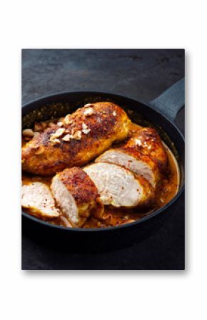 Roasted spicy butter chicken breast fillet in red curry gravy sauce with coconut, lime, and cashew nuts served as close-up in a design frying pan