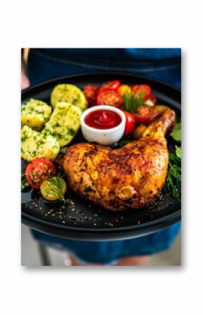 Woman holding plate with roasted chicken leg with boiled potatoes, fresh tomato salad and ketchup 