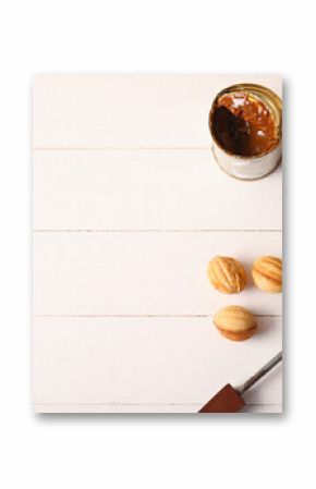 Baking form with tasty walnut shaped cookies and tin can of boiled condensed milk on white wooden background