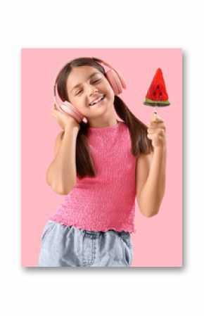 Happy little girl with lollipop in shape of watermelon slice listening music on pink background