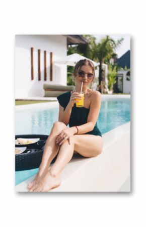 Stylish woman enjoying tropical poolside breakfast with orange juice, reflecting slow luxury morning, feminine energy, wellness lifestyle and modern resort leisure.