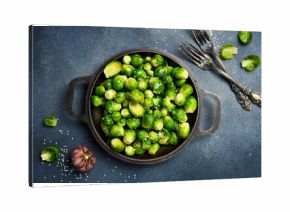 Baked Brussels sprouts with sesame and garlic in a frying pan. Top view, close-up. On a dark textured background.