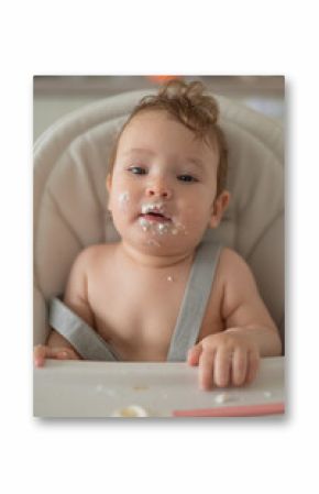 Cute baby boy smeared in sour cream sits in a high chair. 