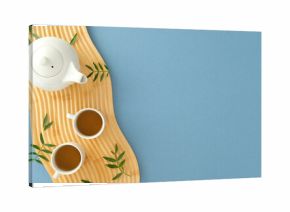 Elegant tea set on wooden tray with green leaves. Minimalist top view against pastel blue.