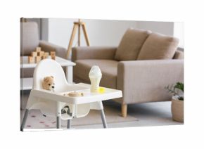 Baby highchair with bottle of milk and toys in living room