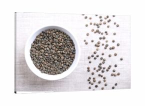 Puy lentils in a white bowl on linen. Dried variety of small lentils, mottled, of slate-gray to dark green color, with blue marbling. Lens esculenta variety, grown in the Auvergne region of France.