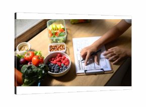 Nutritionist analyzing and writing a healthy meal plan with fresh fruits, vegetables, and nuts on the table