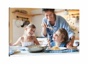 Happy mother and kids eating pasta at home kitchen, having fun, enjoying family lunch, healthy comfort food for children. Homemade Italian cuisine, mac and cheese. Candid, authentic lifestyle moment