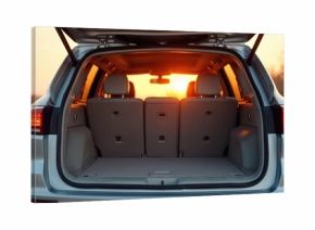 Car trunk open at sunset in a dry landscape. Vehicle is clean and empty, suggesting travel preparation or arrival. Sun shines warmly through rear window.