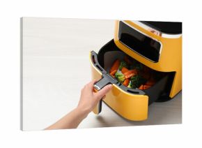 Woman opening air fryer with grilled vegetables at white wooden table, closeup. Space for text