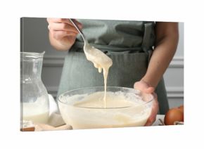 Woman making batter (liquid dough) at white table indoors, closeup