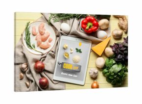 Tablet computer with tasty ingredients on yellow wooden background