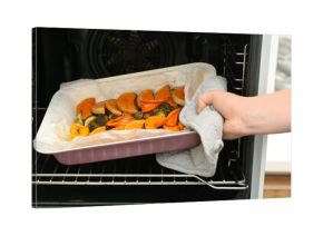 Woman taking baking tray with tasty baked pumpkin, eggplant, bell pepper and zucchini out of oven, closeup