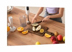 Young woman cutting fresh pear for smoothie in kitchen