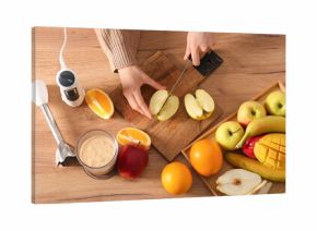 Young woman cutting fresh fruits for smoothie in kitchen