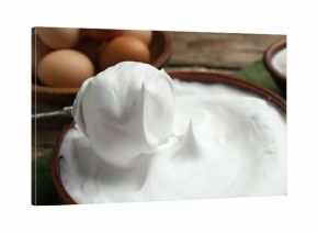 Whipped egg whites in bowl, whisk and ingredients on table, closeup